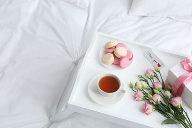 Photo of Tasty breakfast served in bed. Delicious macarons, tea, gift box, flowers and I Love You card on tray, space for text