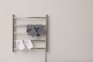 Photo of Heated towel rail with socks on white wall, space for text