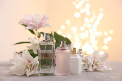 Photo of Perfume bottles and bouquet of beautiful lily flowers on table against beige background with blurred lights, closeup