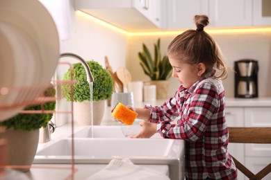 Photo of Little girl washing dishes in kitchen at home