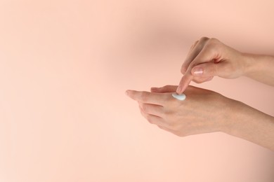 Photo of Woman applying hand cream on pink background, closeup. Space for text