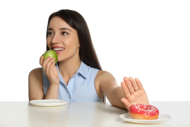 Photo of Woman choosing between apple and doughnut at table on white background