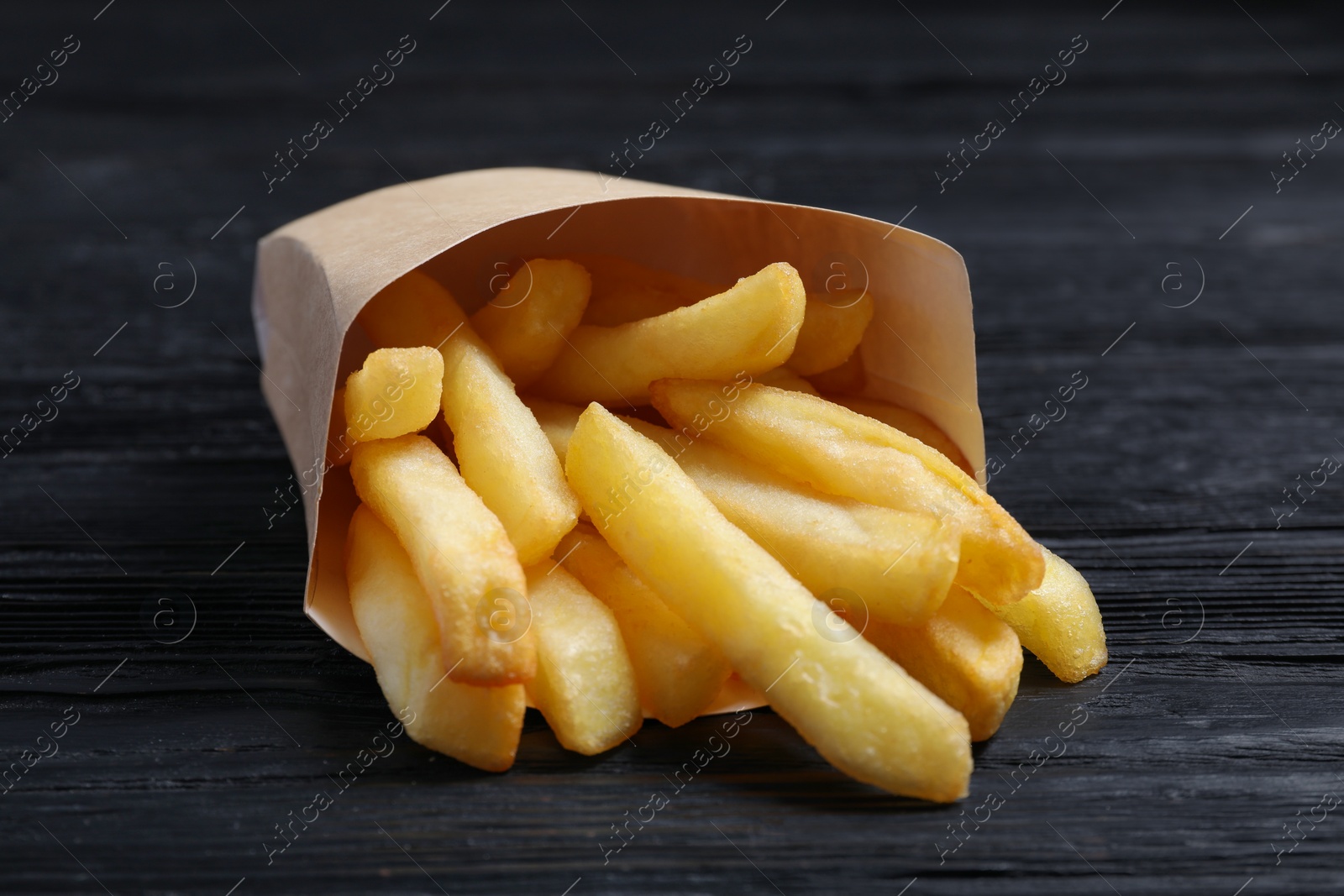 Photo of Delicious french fries in paper box on black wooden table, closeup