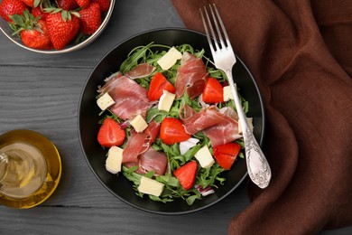 Photo of Tasty salad with brie cheese, prosciutto and ingredients served on grey wooden table, flat lay