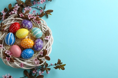 Photo of Flat lay composition with painted Easter eggs and blossoming branches on color background, space for text