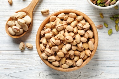 Photo of Composition with organic pistachio nuts in bowl on wooden table, top view
