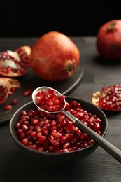 Photo of Tasty ripe pomegranates and grains on dark wooden table