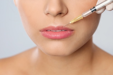 Photo of Young woman getting lips injection on grey background, closeup. Cosmetic surgery