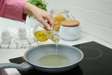 Photo of Woman pouring oil from jug into frying pan in kitchen, closeup