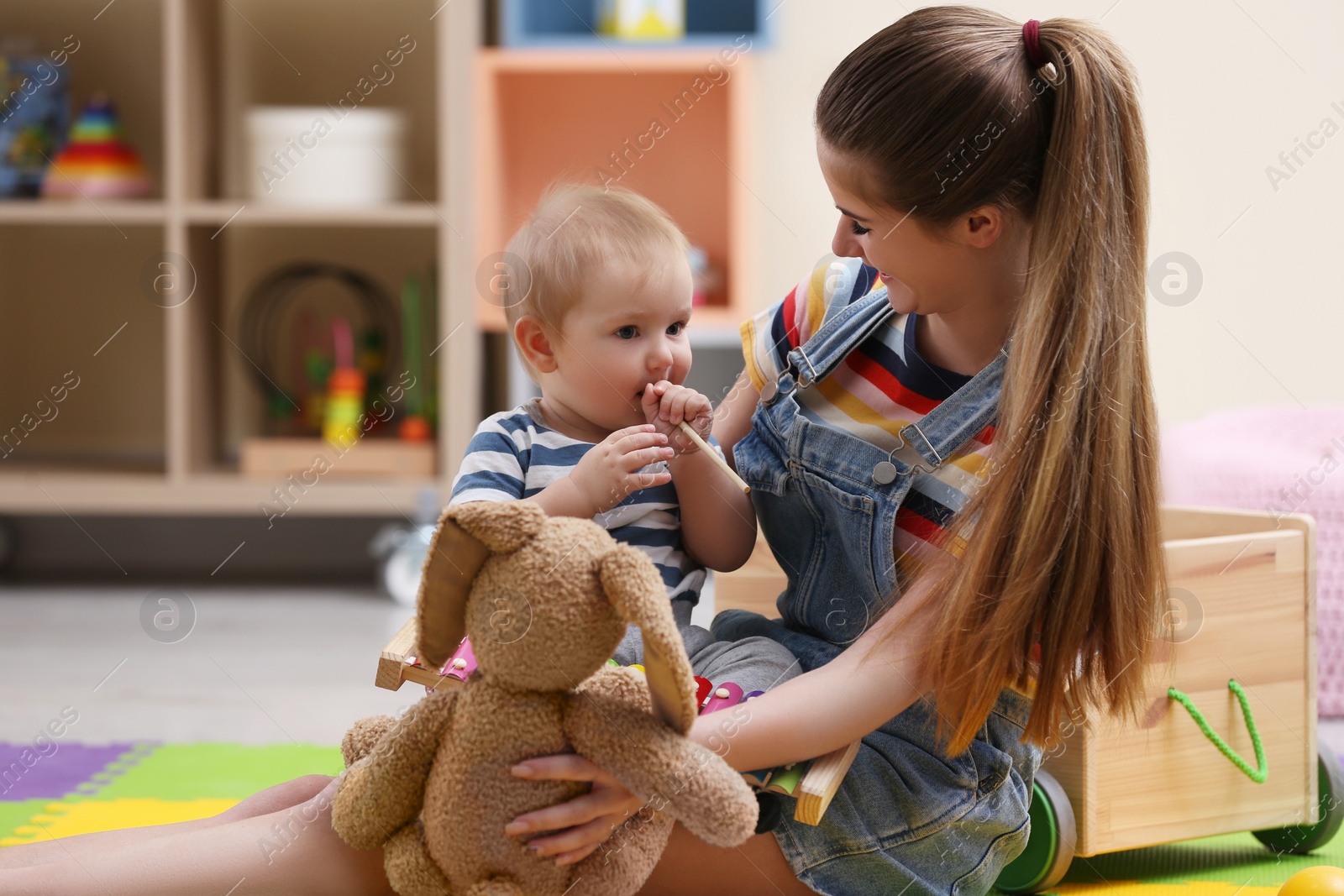 Photo of Teen nanny and cute little baby playing with toys at home