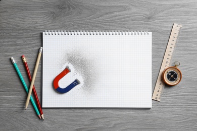 Notebook, stationery, compass and magnet with iron powder on wooden table, flat lay. Space for text