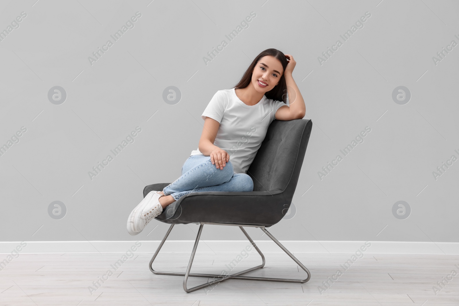 Photo of Beautiful woman sitting in armchair near light grey wall indoors