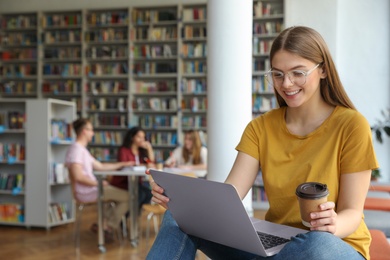 Photo of Young woman working on laptop in library. Space for text
