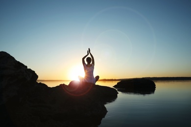 Photo of Woman practicing yoga near river on sunset. Healing concept