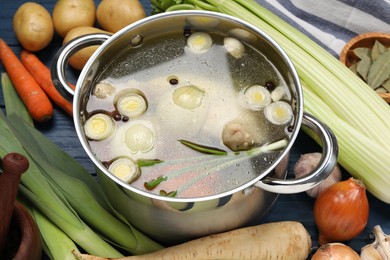 Photo of Pot with tasty bouillon and different ingredients on blue wooden table