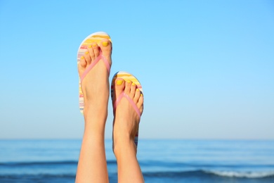 Photo of Closeup of woman wearing flip flops near sea, space for text. Beach accessories