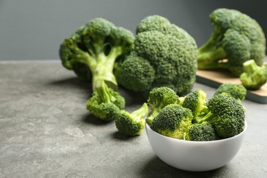 Photo of White bowl of fresh green broccoli on grey stone table, space for text