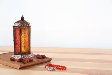Photo of Muslim lantern Fanous, dried dates and prayer beads on table against light background. Space for text