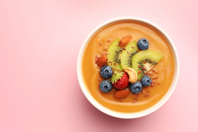 Photo of Delicious smoothie bowl with fresh berries, kiwi and nuts on pale pink background, top view. Space for text