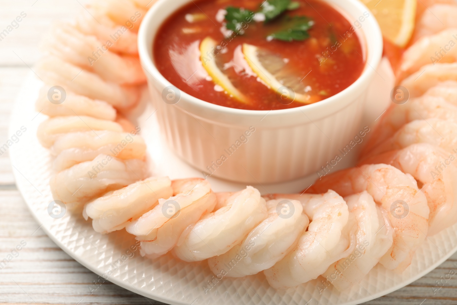 Photo of Tasty boiled shrimps with cocktail sauce and lemon on white wooden table, closeup