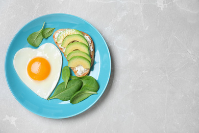 Photo of Romantic breakfast with heart shaped fried egg on light grey table, top view. Space for text