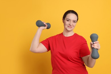 Photo of Happy overweight woman doing exercise with dumbbells on orange background, space for text