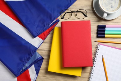 Photo of Learning foreign language. Different books, flag of United Kingdom, stationery and glasses on wooden table, flat lay