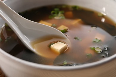 Delicious miso soup with tofu and spoon in bowl, closeup