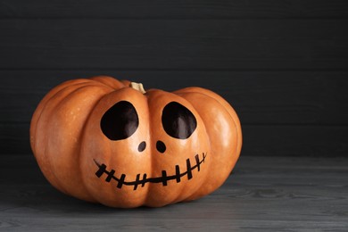 Photo of Pumpkin with drawn spooky face on grey table, space for text. Halloween celebration