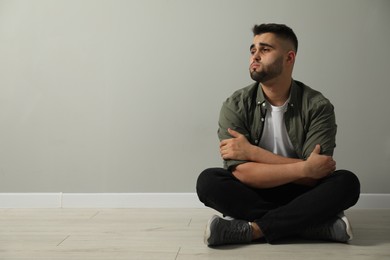 Photo of Sad man sitting on floor near light grey wall. Space for text