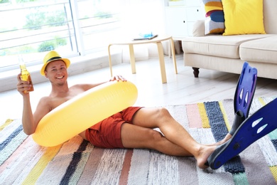 Photo of Shirtless man with inflatable ring and bottle of drink wearing flippers on floor at home