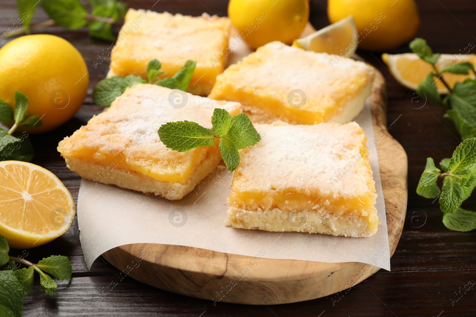 Photo of Tasty lemon bars with powdered sugar and mint on wooden table, closeup