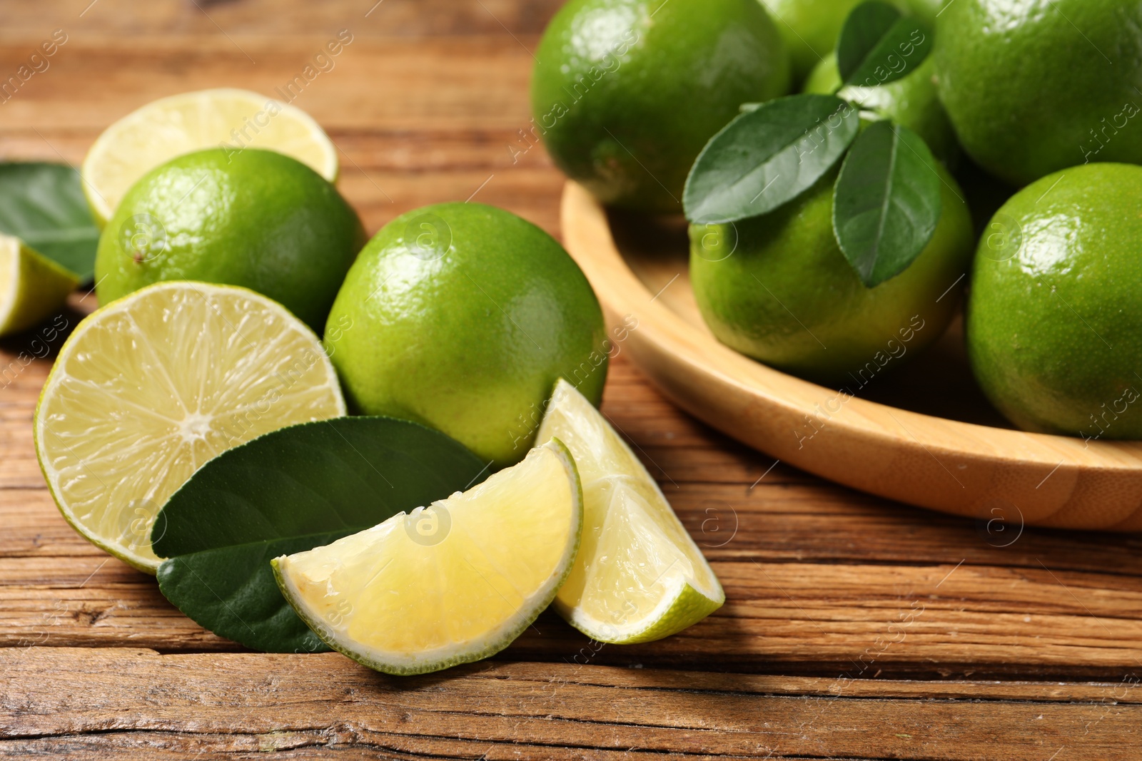 Photo of Fresh ripe limes and green leaves on wooden table, closeup