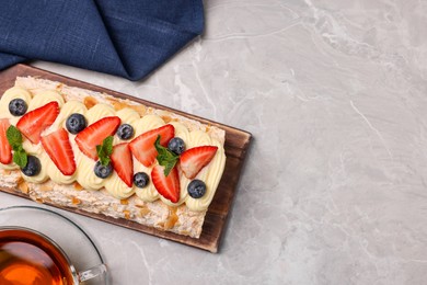 Photo of Tasty meringue roll with cream, strawberry, blueberry, mint and tea on light grey marble table, flat lay. Space for text