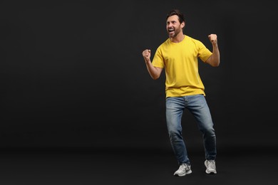Photo of Emotional sports fan celebrating on black background, space for text