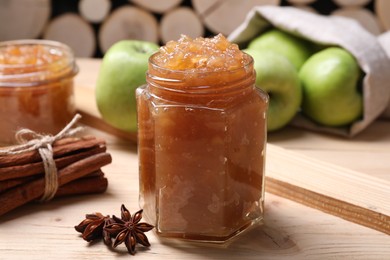 Photo of Delicious apple jam in jars, fresh fruits and spices on wooden table