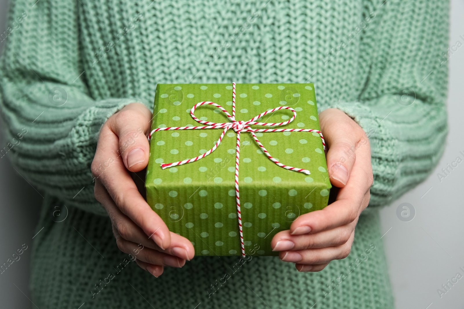 Woman holding green Christmas gift box on grey background, closeup Photo of Woman holding green Christmas gift box on grey background, closeup