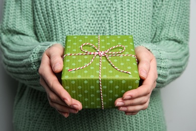 Woman holding green Christmas gift box on grey background, closeup