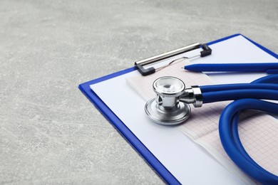 Photo of Clipboard with stethoscope and cardiogram on grey table, closeup. Space for text