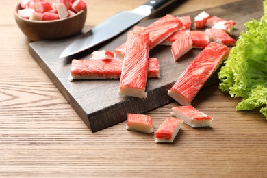 Photo of Delicious crab sticks with lettuce on wooden table, closeup
