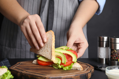 Photo of Woman making tasty sandwich with avocado at black table, closeup