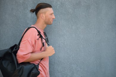 Photo of Handsome young man with stylish sunglasses and bag near grey wall, space for text