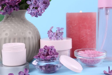 Photo of Cosmetic products and lilac flowers on light blue background, closeup