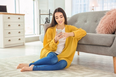 Photo of Attractive young woman using mobile phone on floor near sofa