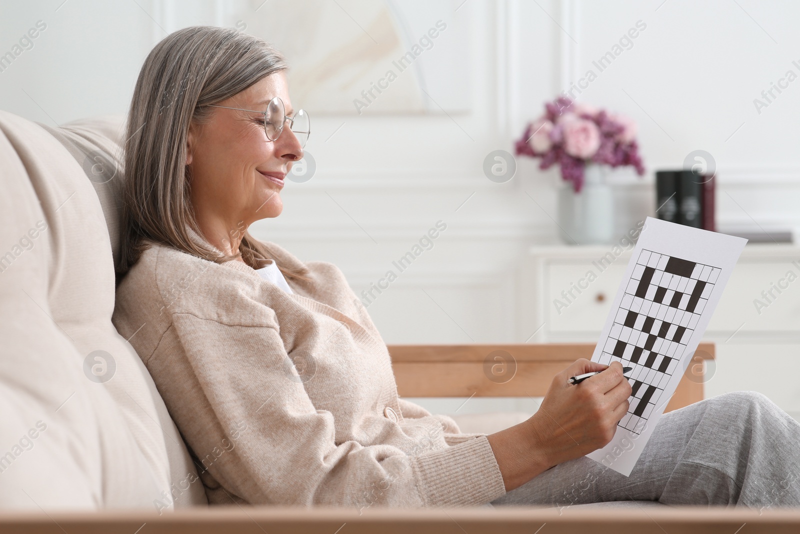 Photo of Senior woman solving crossword on sofa at home