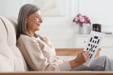 Senior woman solving crossword on sofa at home