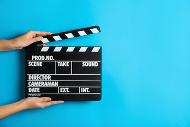 Photo of Woman holding clapperboard on light blue background, closeup with space for text. Cinema production