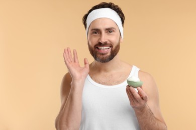 Photo of Man with headband washing his face using sponge on beige background