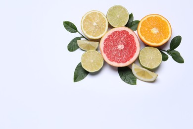 Photo of Different cut citrus fruits and leaves on white table, flat lay. Space for text