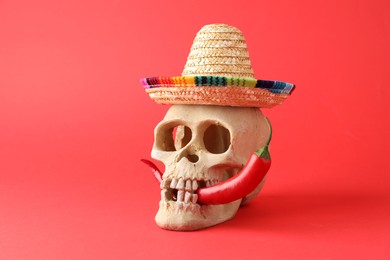 Photo of Human scull with Mexican sombrero hat and hot chili pepper on red background